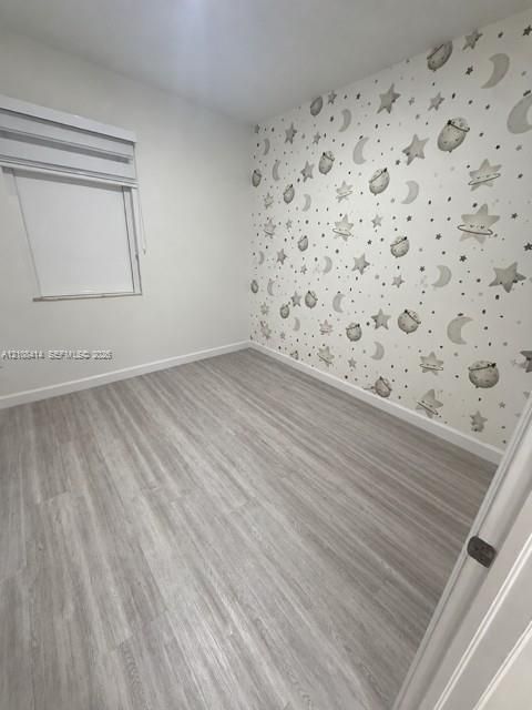 Room featuring wood-finish flooring, a feature wall with celestial-patterned wallpaper, and a window with a retractable roller shade