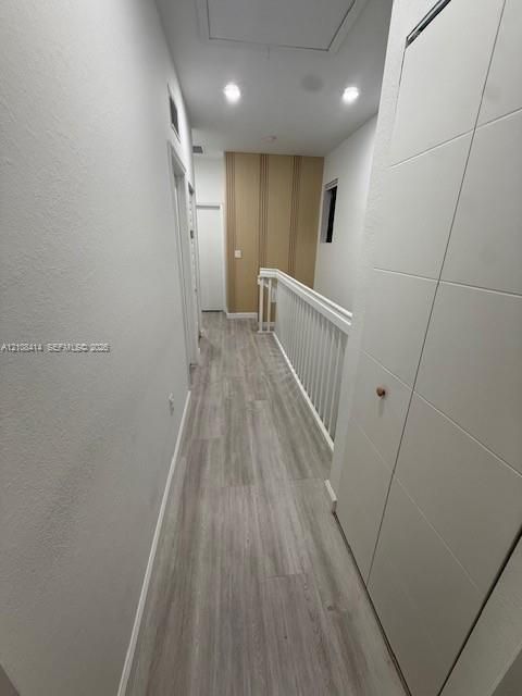 Hallway featuring wood-finish flooring, recessed lighting, white panel doors, and a vertical-slat accent wall with a white balustrade