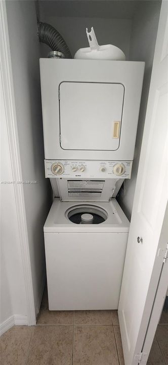 Built-in stacked laundry unit with top-loading washer and neutral tile flooring