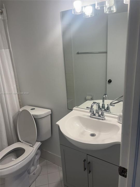Bathroom featuring a grey shaker-style vanity, white integrated sink, polished chrome faucet, large wall-mounted mirror, and three-light overhead fixture