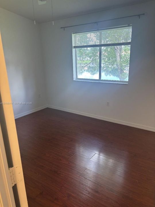 Room featuring wood-finish flooring, a ceiling fan, and a window with water backdrop