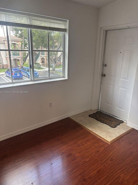 Entryway featuring wood-finish flooring, a neutral-toned tile threshold, a six-panel door, and a large window with fitted blinds