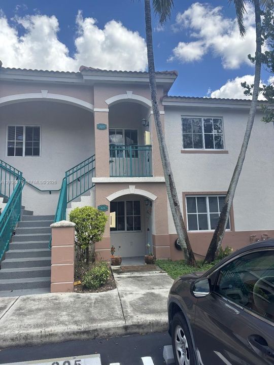 Two-story exterior featuring a neutral stucco facade, arched architectural detailing, metal railings, and an upper-level balcony