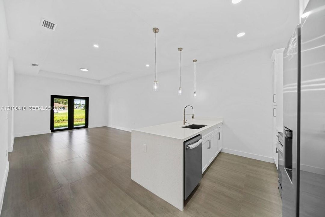 Kitchen featuring a waterfall-edge quartz island, stainless steel undermount sink, pendant lighting, wood-finish flooring, and black-framed French doors