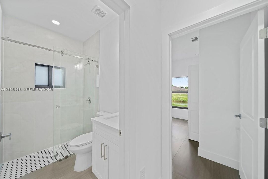 Bathroom featuring a glass-enclosed shower with a black and white tiled floor, vanity cabinet with a stone-surface countertop, recessed lighting, and wood-finish flooring
