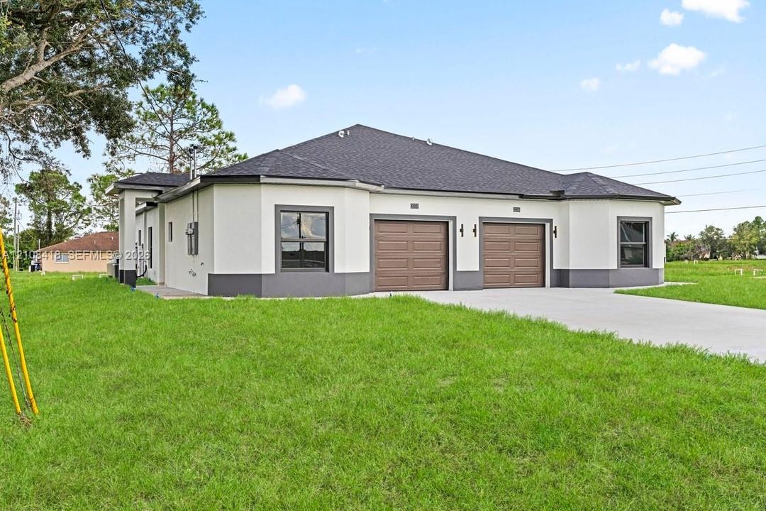 Stucco exterior featuring dual-bay garage doors, a concrete driveway, multi-faceted roofline, and trimmed windows