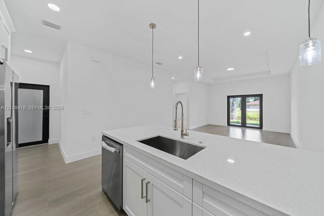 Kitchen island featuring white shaker-style cabinetry, quartz countertops, an undermount stainless steel sink, and a gooseneck faucet, accented by glass pendant lighting and light-toned wood-finish flooring