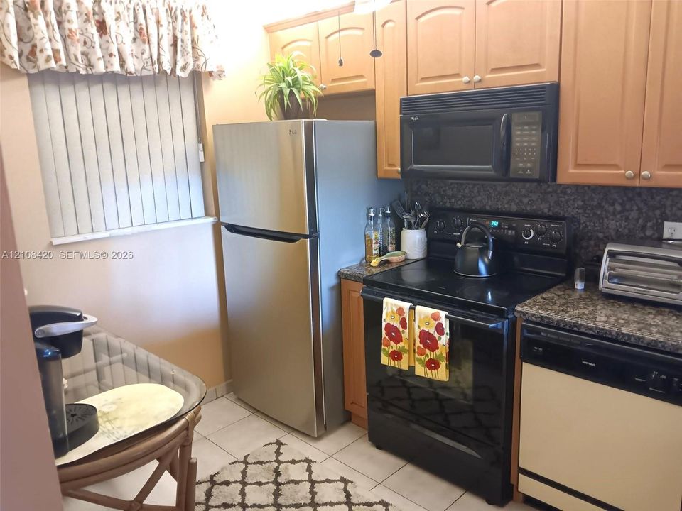 Kitchen featuring natural wood-finish cabinetry, stone-texture countertops, tile flooring, and integrated black appliances
