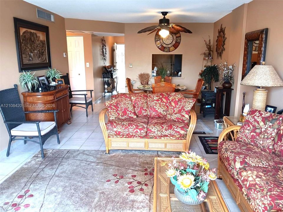 Open-concept floor plan featuring neutral tile flooring, a decorative wall-mounted ceiling fan with light fixture, and an interior pass-through window