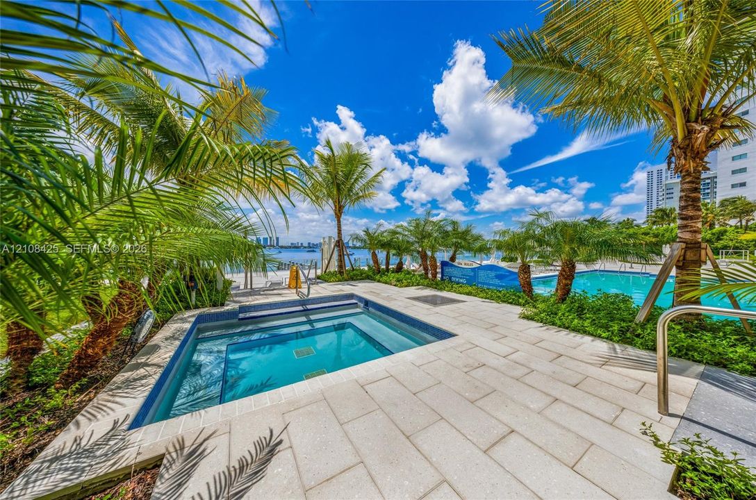 In-ground spa with stone-tile surround, swimming pool, palm-lined landscaping, and water-front placement
