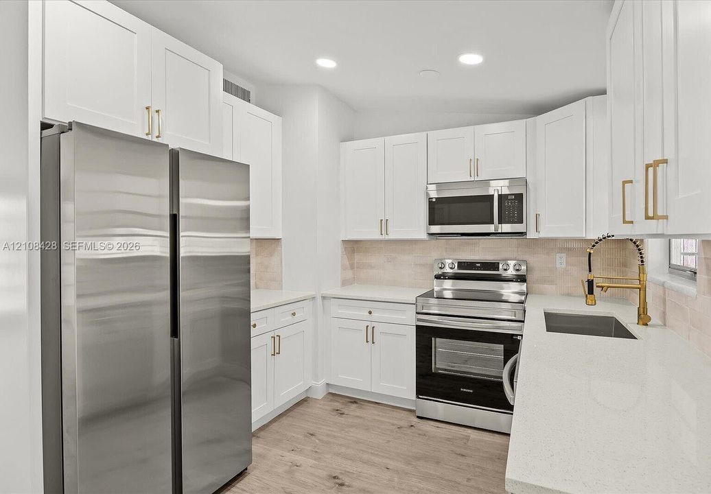 Kitchen featuring white shaker-style cabinetry with gold-tone hardware, stone countertops, stainless steel appliances, wood-finish flooring, and a gooseneck faucet