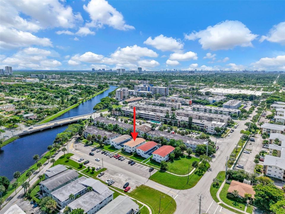 Aerial perspective of the residential complex featuring multi-story structures, integrated parking areas, manicured green space, and proximity to a waterway