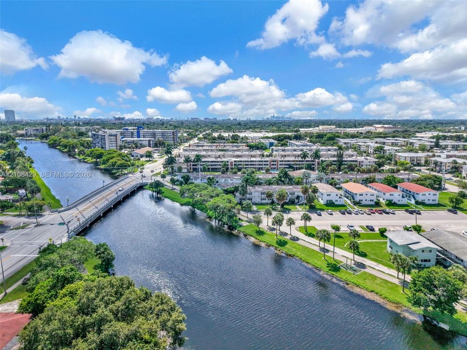 Aerial perspective of a waterway featuring mature palm trees, landscaped green space, and proximity to infrastructure