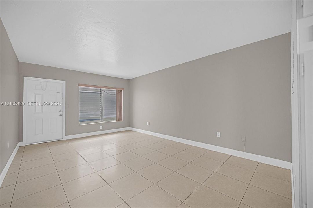 Neutral interior featuring large-format tile flooring, light-toned wall paint, a multi-pane window, and an exterior-grade entry door