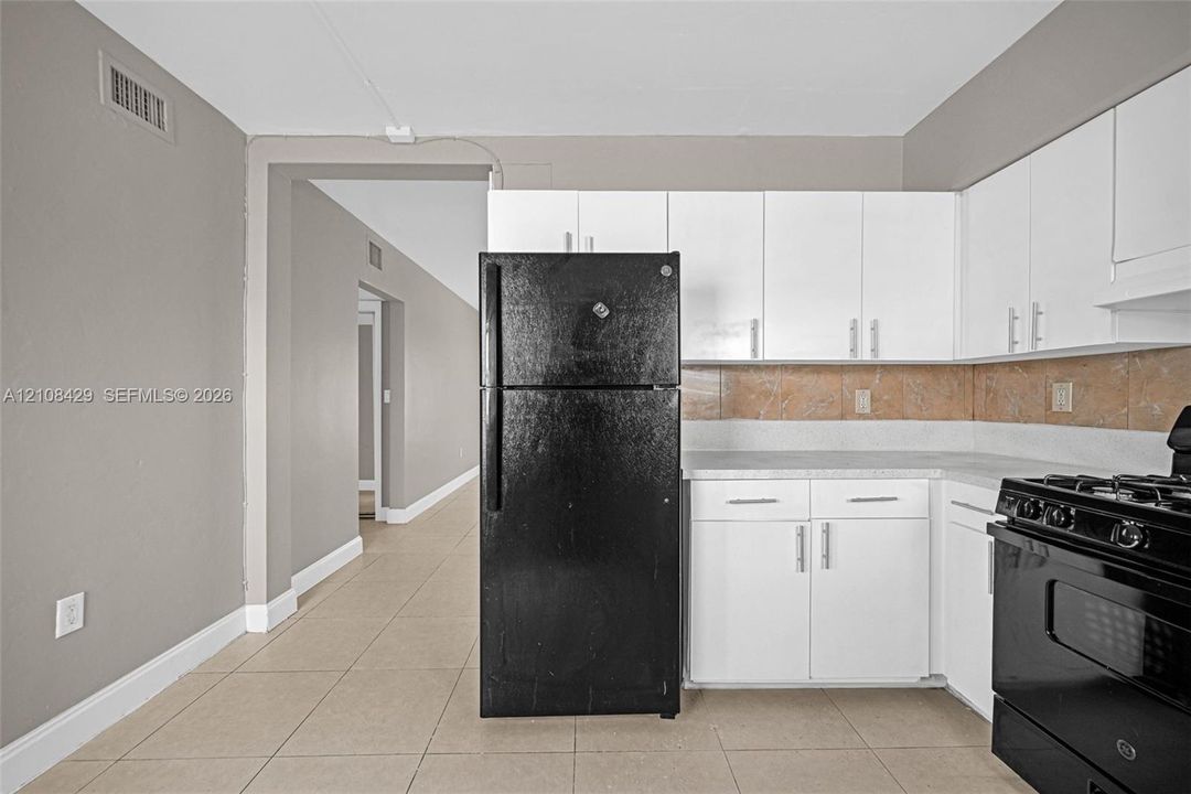 Kitchen featuring white shaker-style cabinetry, matte black appliances, neutral tile flooring, and a stone-tiled backsplash