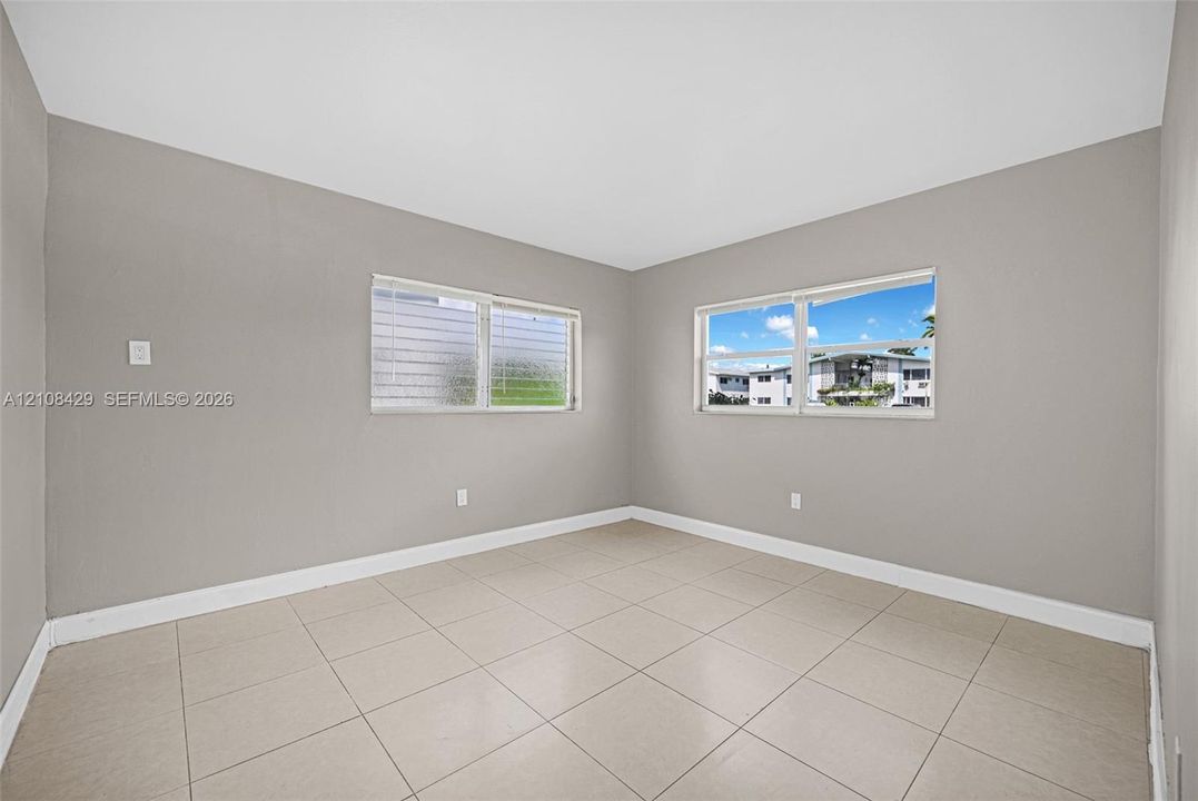 Neutral-toned interior space featuring light-colored ceramic tile flooring, neutral wall paint, and dual windows with adjustable jalousie-style glass panes