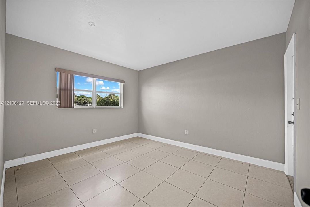 Neutral-toned interior space featuring light-colored ceramic tile flooring, smooth walls, and a window with horizontal blinds