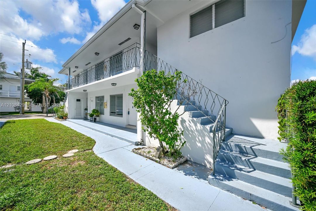 Exterior facade featuring a painted stucco finish, wrought-iron staircase and balcony railings, covered walkway, and manicured lawn