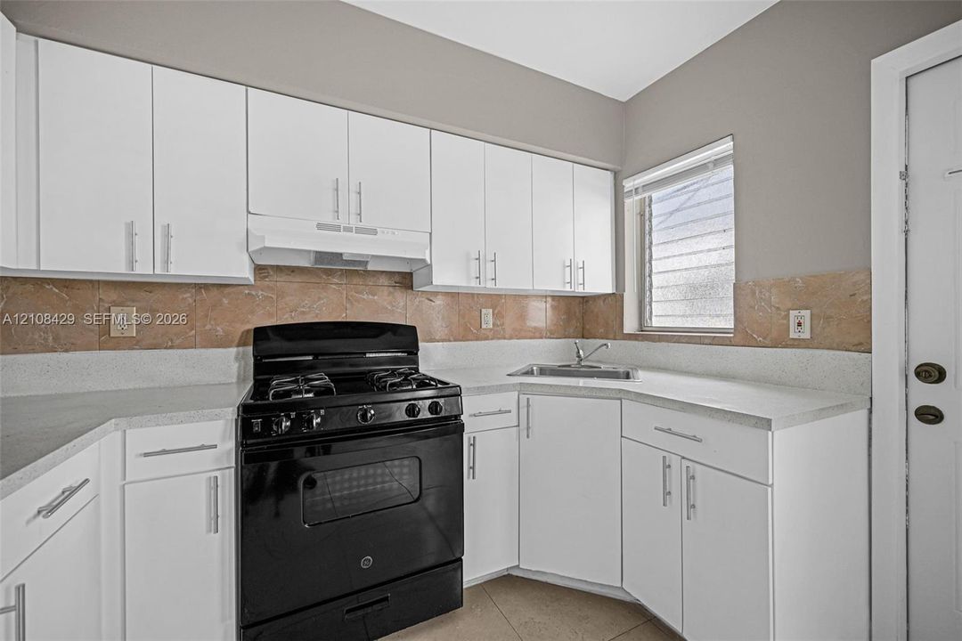 Kitchen featuring white cabinetry, solid-surface countertops, stone-finish backsplash, and a black range
