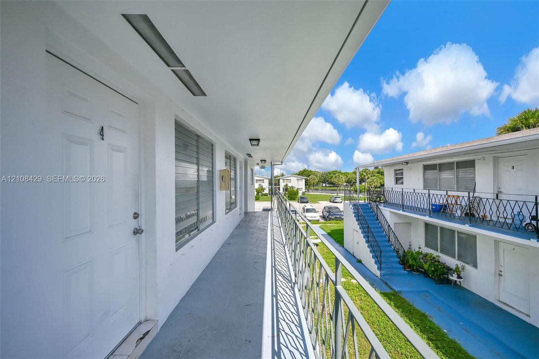 Exterior walkway featuring white painted stucco finish, horizontal sliding windows, flush-mount ceiling lighting, and black metal railings