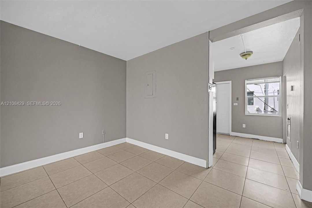 Neutral-toned interior featuring large-format ceramic tile flooring, matte grey wall finishes, and a single-pane window with a horizontal blind