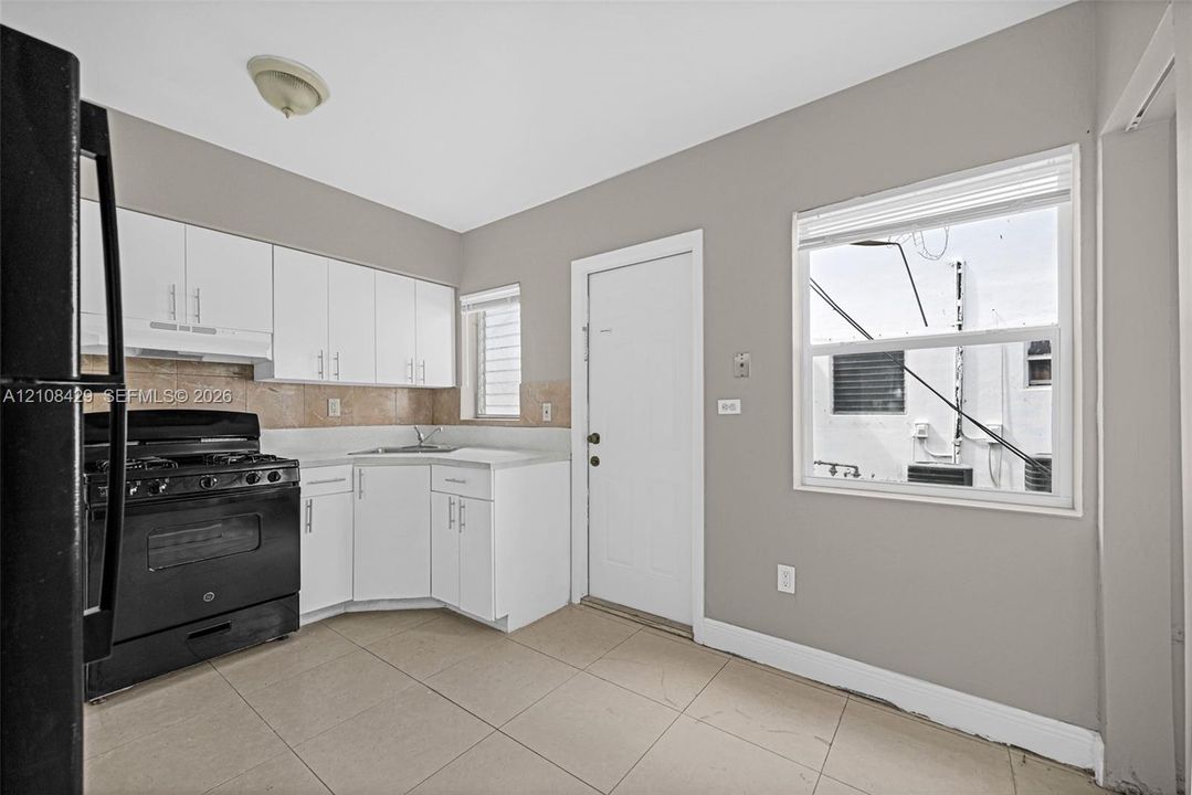 Kitchen featuring white cabinetry, tile flooring, stone-finish backsplash, and black appliances