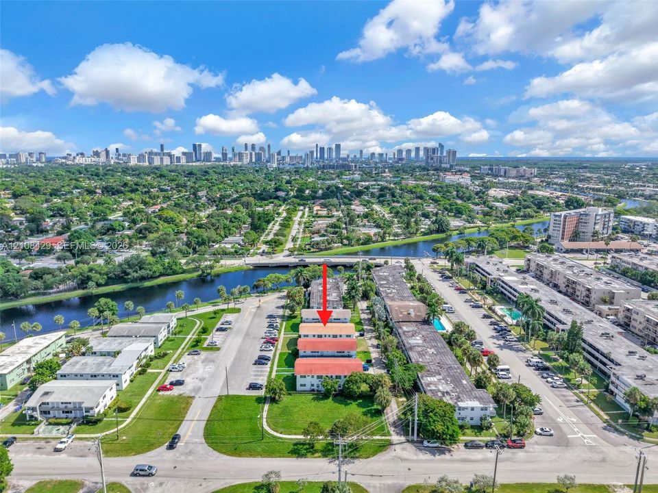 Aerial perspective featuring a multi-unit residential building with a red tile roof, surrounded by green space, paved parking, and a canal