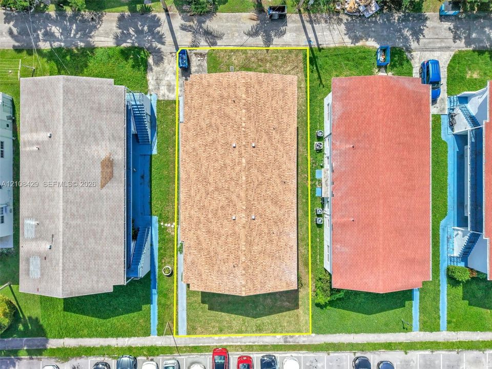 Aerial perspective of property lot featuring asphalt shingle roof, grass-covered grounds, and paved driveway access