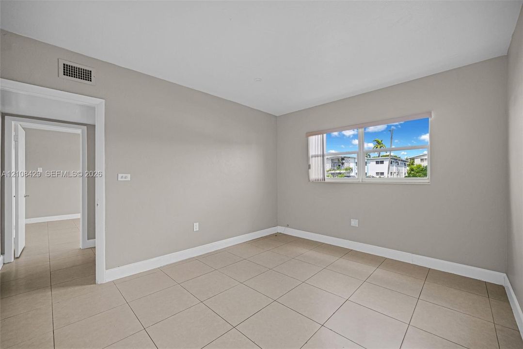 Neutral-toned interior space featuring light-colored tile flooring, smooth walls, and a large window with horizontal blinds