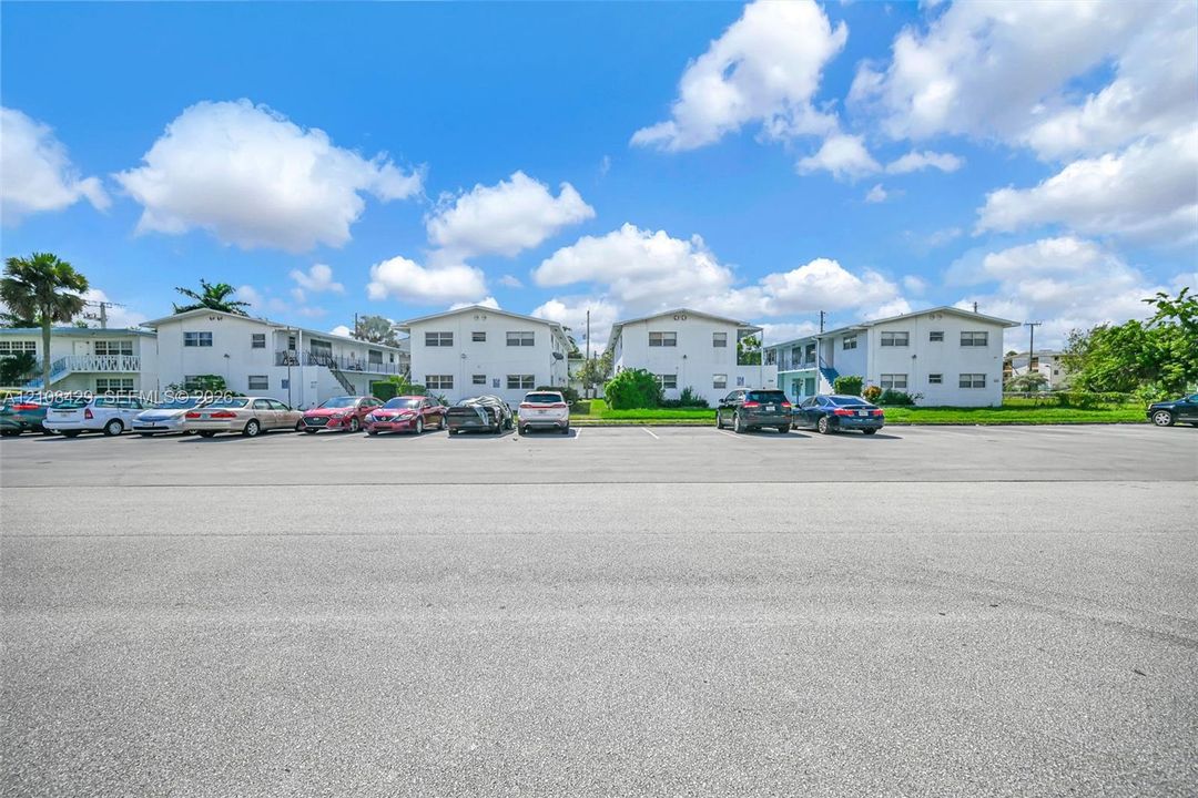 Multi-story residential complex featuring white stucco facades, flat roofs, and dedicated asphalt surface parking