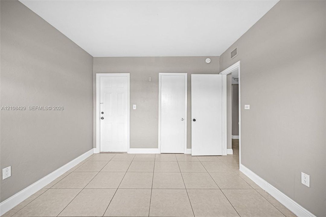 Neutral-toned interior room featuring large-format ceramic tile flooring, three white paneled doors, and smooth, light-grey wall finishes