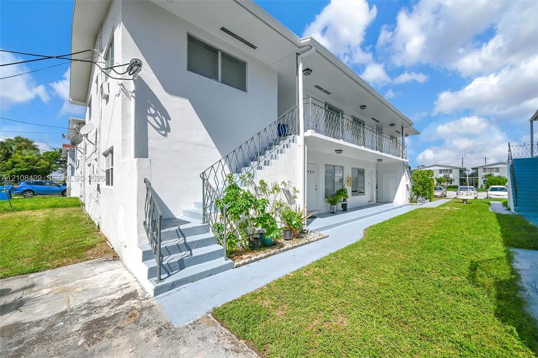 Two-story exterior featuring a smooth stucco facade, metal railing, exterior staircase, and a covered balcony