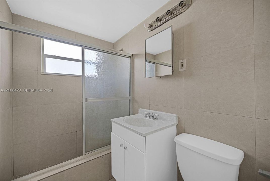 Bathroom featuring floor-to-ceiling tile, single-basin vanity with a stone-finish countertop, sliding glass shower enclosure, and rectangular mirrored medicine cabinet