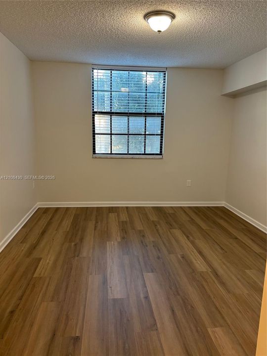 Room featuring wood-finish flooring, a multi-pane window with integrated blinds, and a flush-mount ceiling light fixture