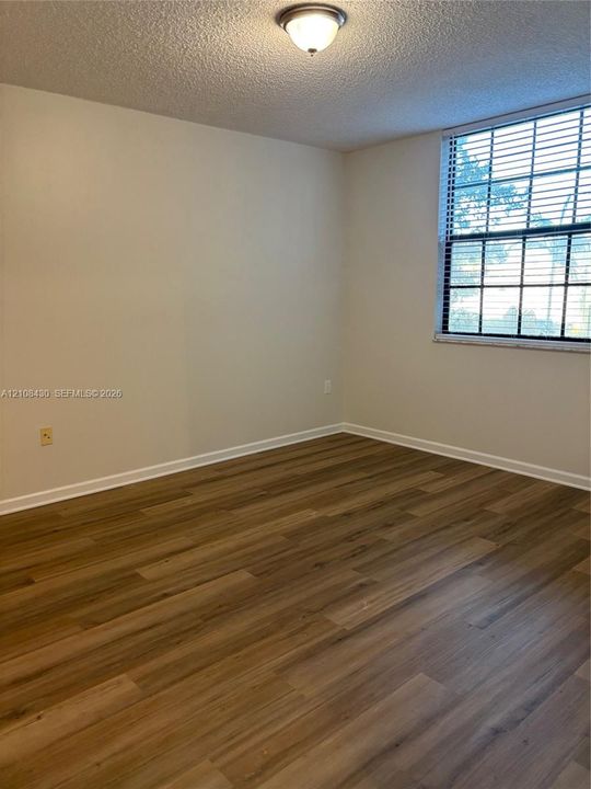 Room featuring wood-finish flooring, a multi-pane window with installed blinds, and a flush-mount ceiling fixture