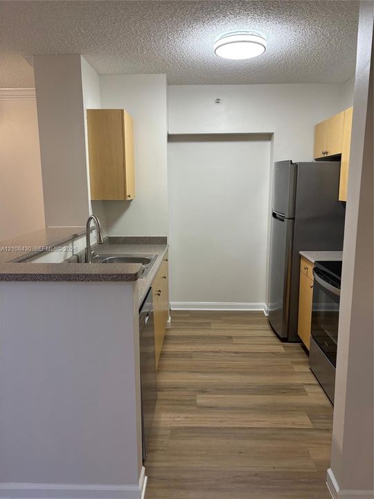 Kitchen featuring wood-finish flooring, stainless steel appliances, light-toned wood cabinetry, stone-composite countertops, and an integrated double-basin sink