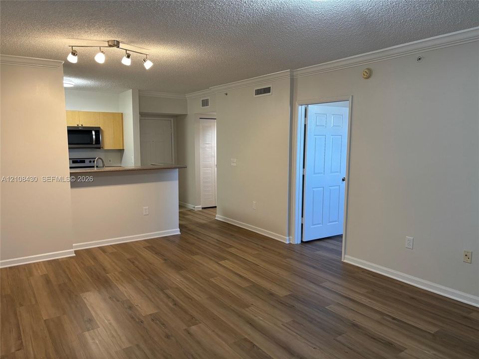 Wood-finish flooring, kitchen with peninsula, built-in microwave, multi-light track fixture, and six-panel interior doors