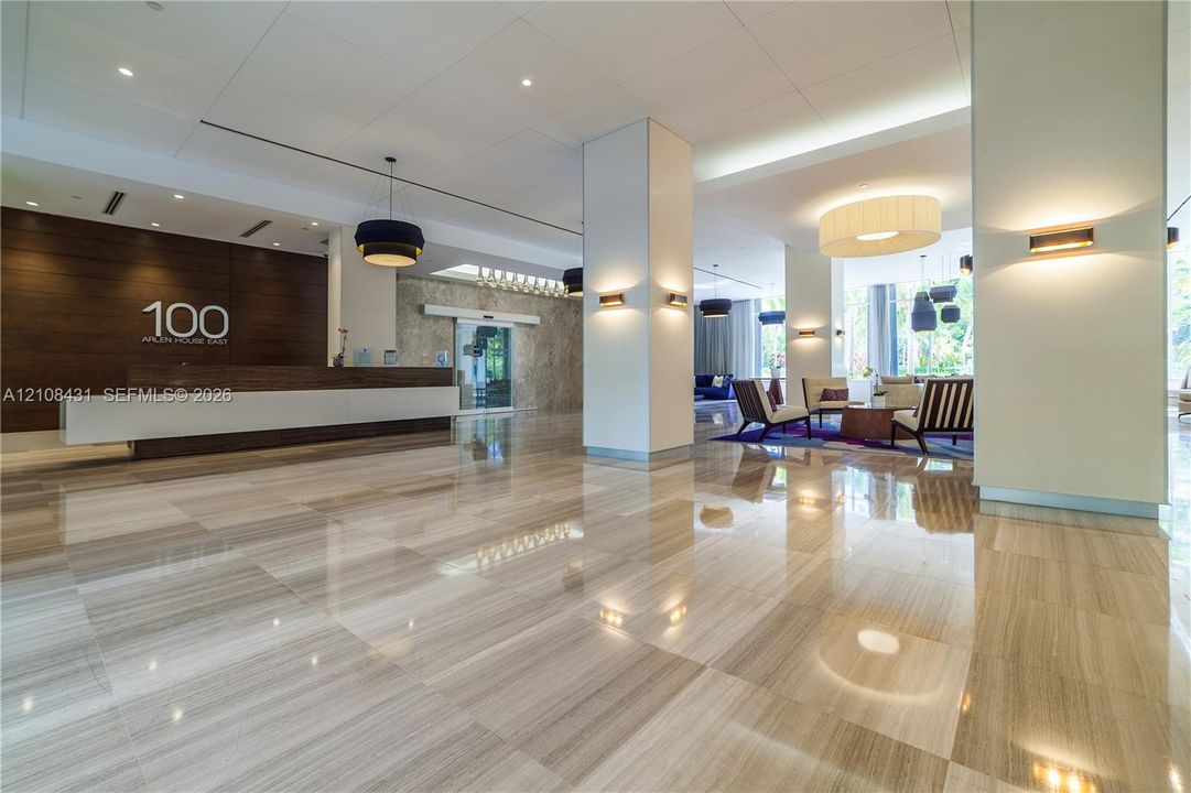 Expansive lobby featuring polished stone flooring, wood-paneled reception desk, structured support columns, and layered architectural lighting