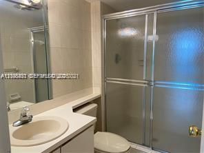 Bathroom featuring a solid-surface vanity countertop with an integrated basin, chrome-finish faucet, full-width vanity mirror, and a walk-in shower enclosure with sliding glass doors and tiled surround