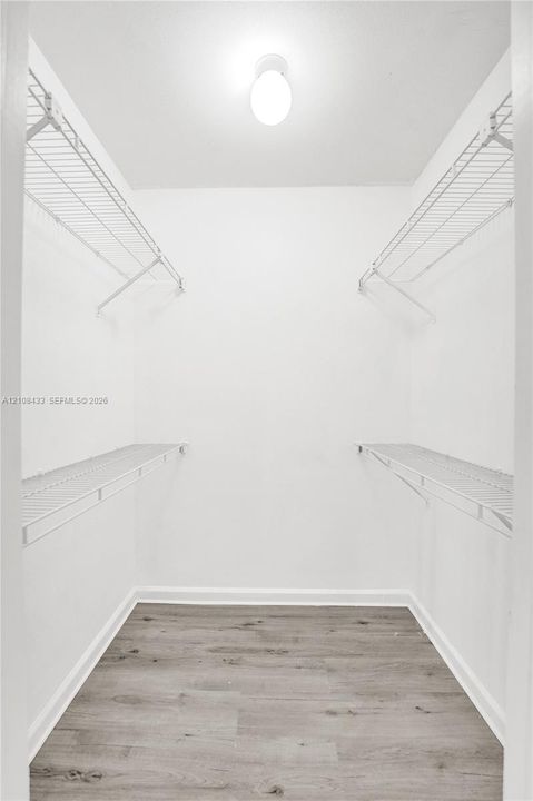 Walk-in closet featuring dual-level white wire shelving, flush-mount dome lighting, and wood-finish flooring