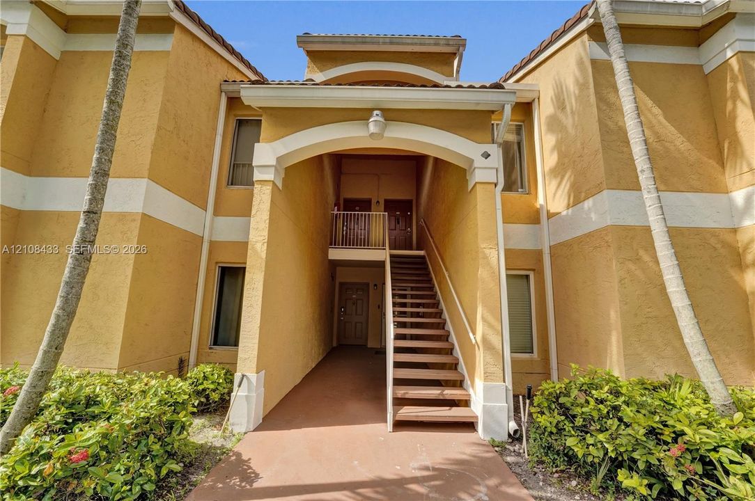 Stucco exterior featuring an arched entryway, decorative trim, tiled roofline, and exterior staircase