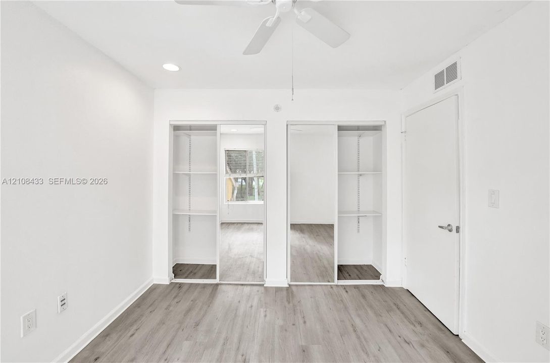 Wood-finish flooring, dual closets with sliding mirrored doors, built-in shelving, and a ceiling fan