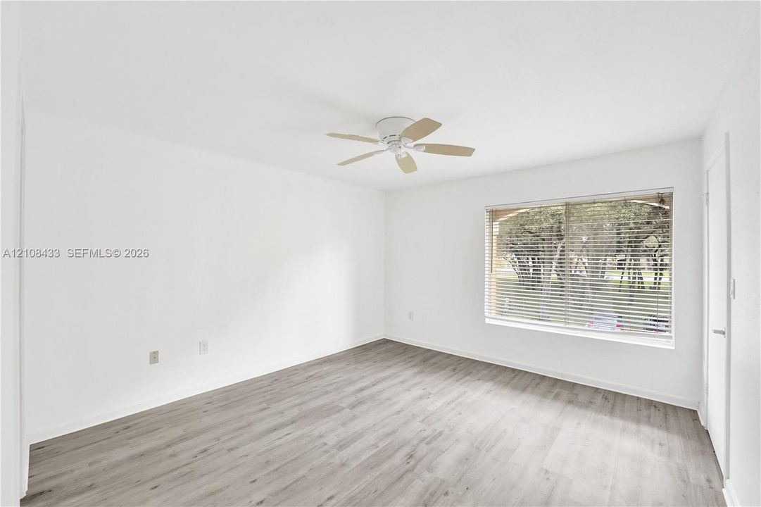 Neutral-toned walls, wood-finish flooring, ceiling-mounted fan, and a large window with horizontal blinds