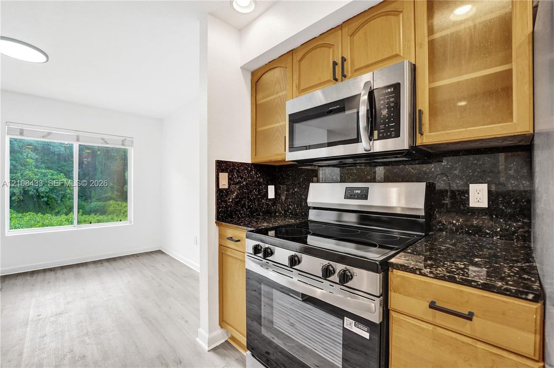 Kitchen featuring wood cabinetry, stainless steel appliances, dark stone countertops, and wood-finish flooring