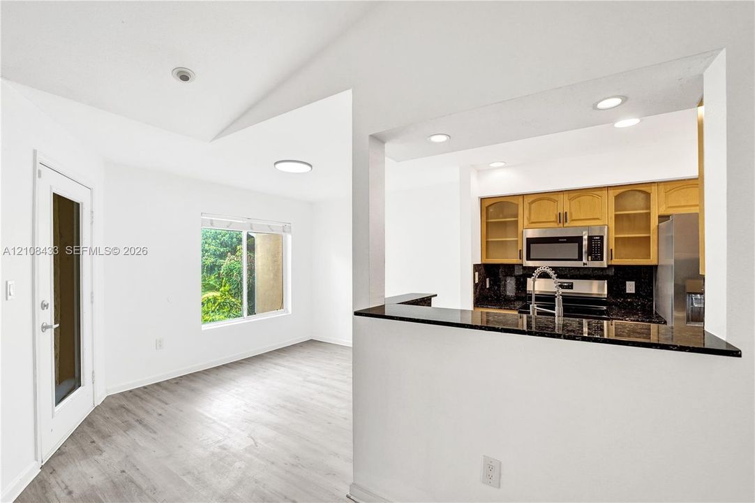 Kitchen featuring wood-finish cabinetry, stone-surface counters, and built-in stainless steel appliances, accented by wood-finish flooring, vaulted ceilings, and recessed lighting