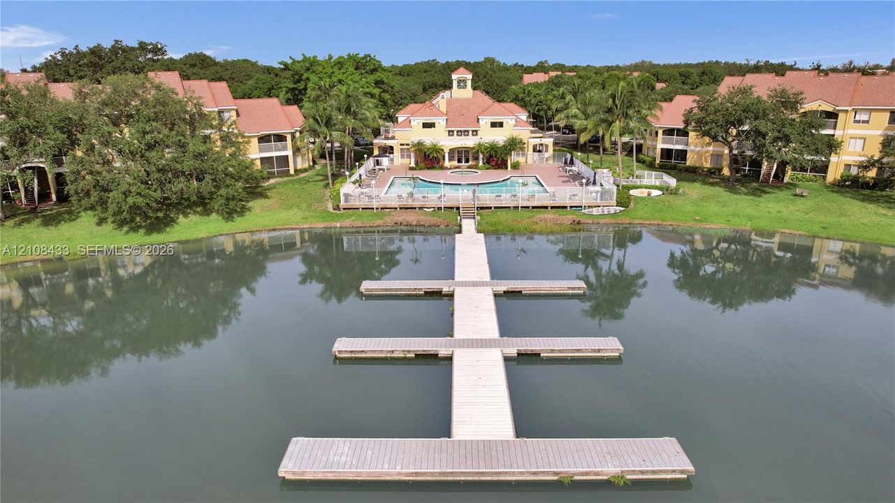 Multi-story residential complex featuring a swimming pool, tiled roof architecture, manicured green space, and a private dock extending into a lake