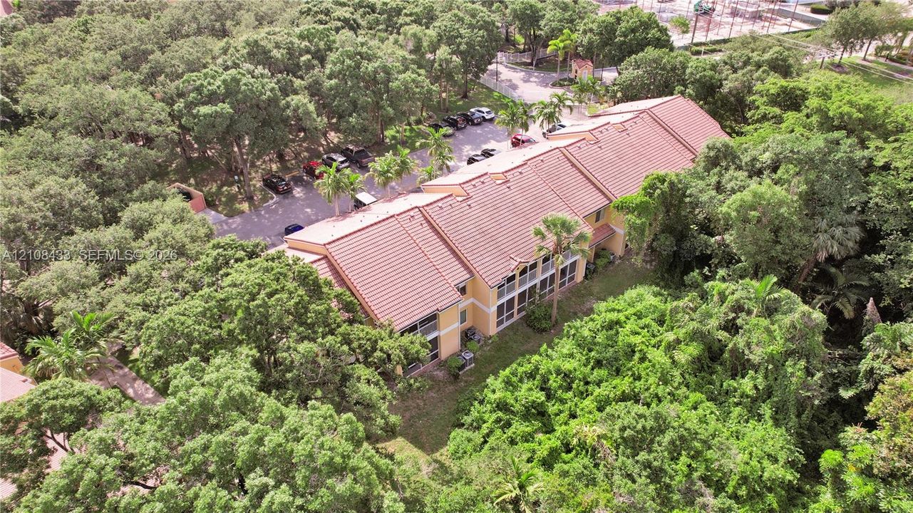 Multi-story residential building featuring a tile roof, light-toned exterior finish, screened balconies, and extensive surrounding tree canopy
