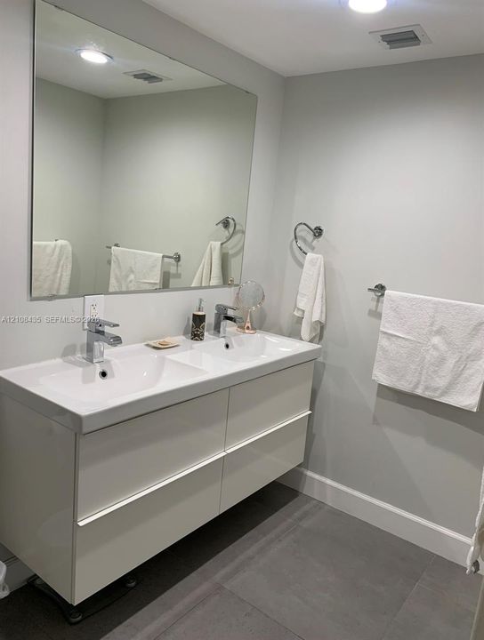 Floating double vanity with integrated dual sinks, polished chrome faucets, large wall-mounted mirror, and tile flooring