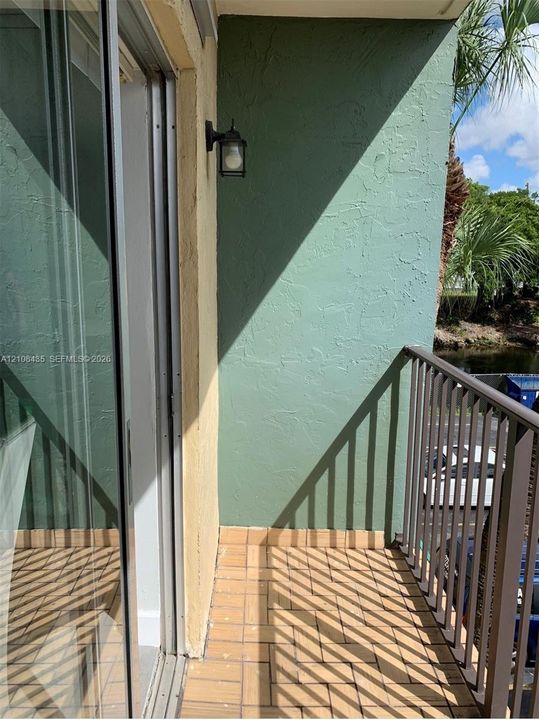 Private balcony featuring textured stucco walls, tiled flooring, metal railing, and a wall-mounted light fixture