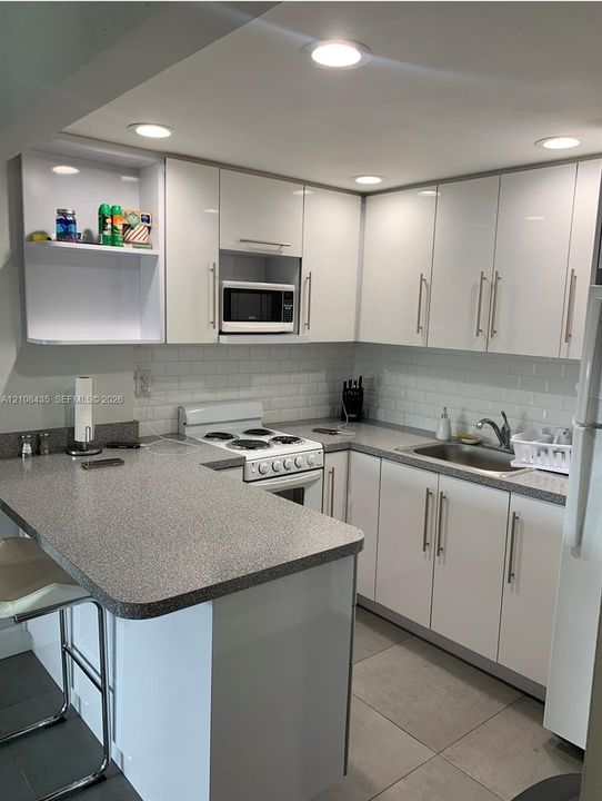 Kitchen featuring white cabinetry, subway tile backsplash, solid-surface countertops, integrated lighting, and tile flooring